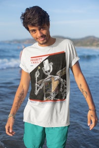 a man standing on the beach wearing a t - shirt with an image of a skeleton